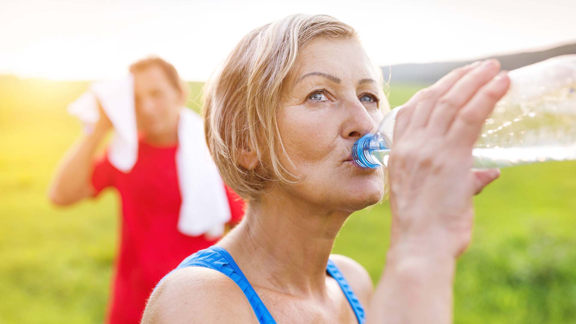 A woman takes a long drink from her water bottle after exercising.
