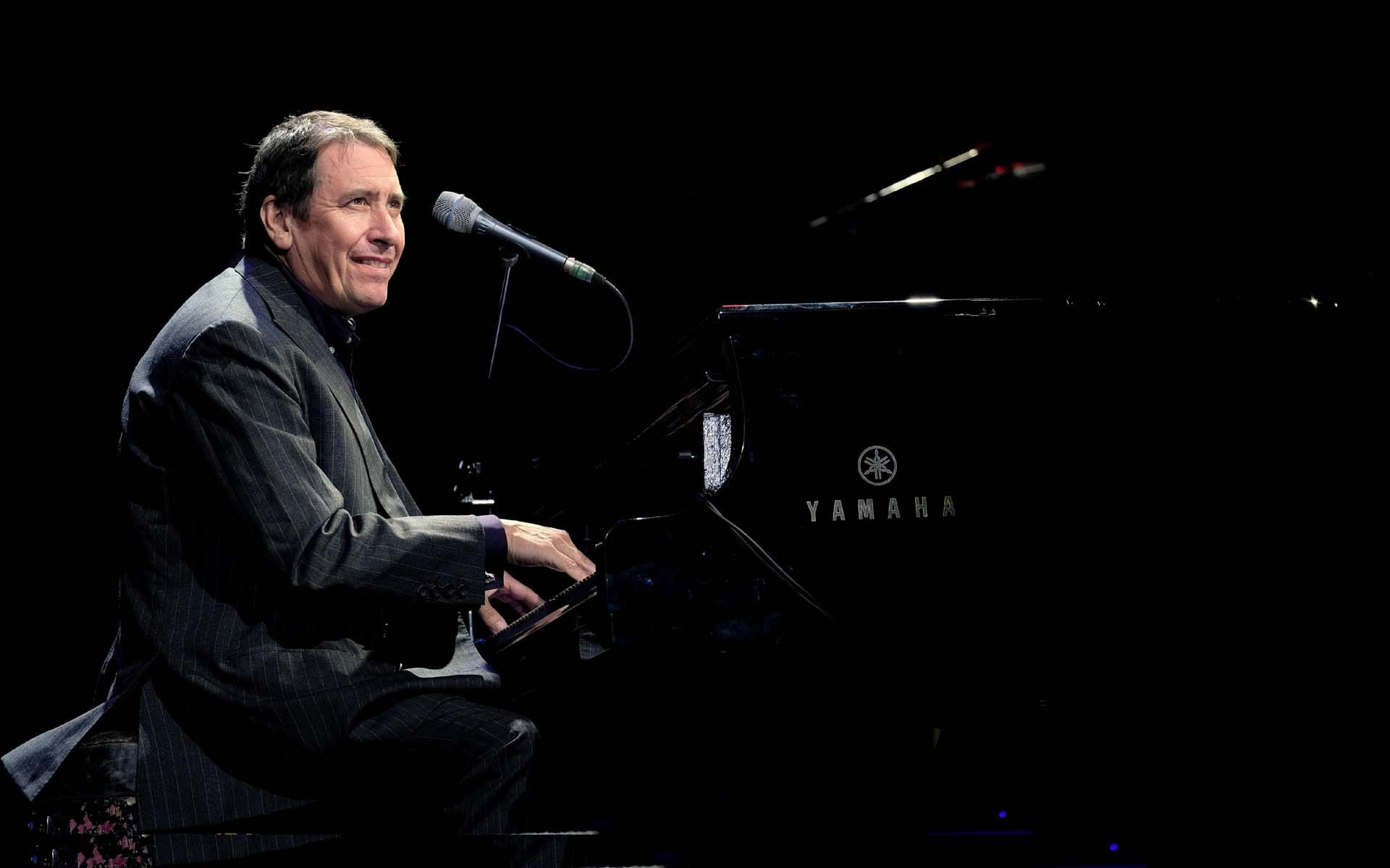 Musician Jools Holland playing a piano with a black backdrop