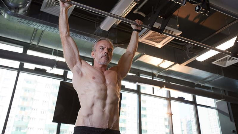man doing a dead hang from the bars
