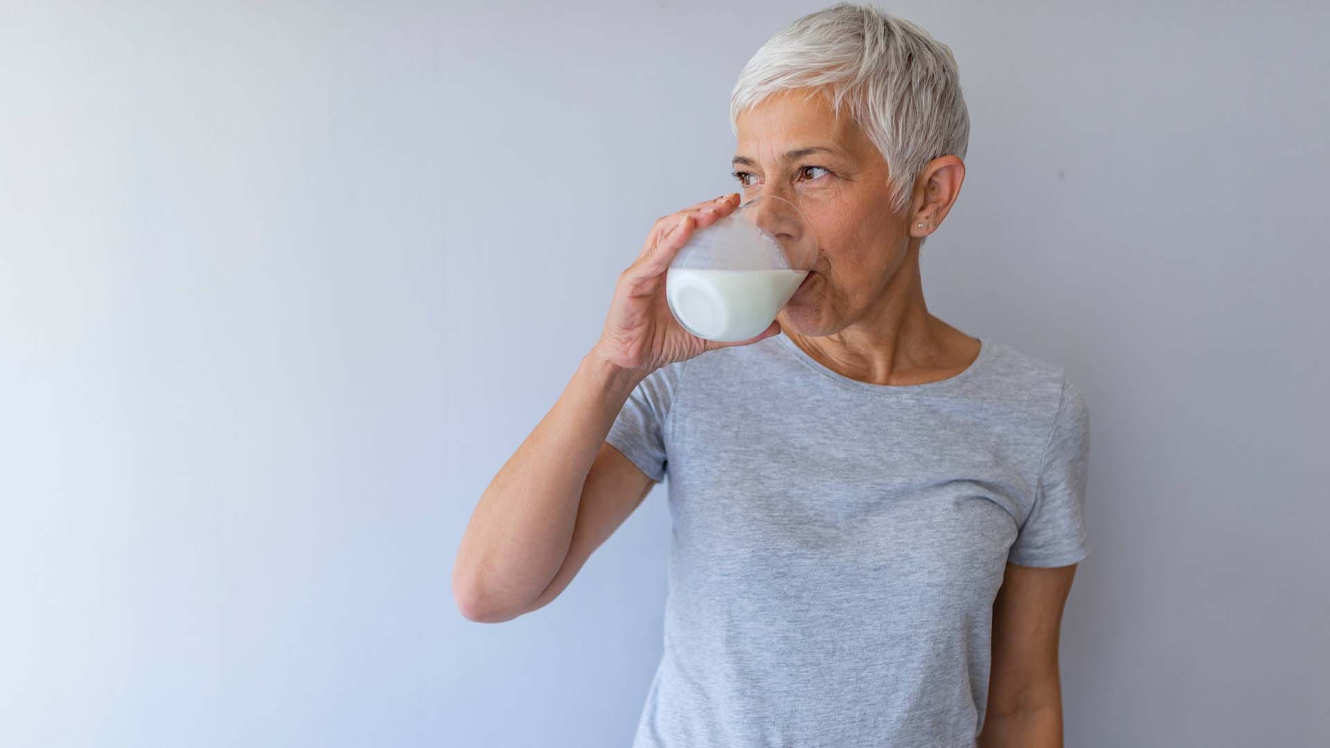 A woman with cropped white hair drinks a glass of milk