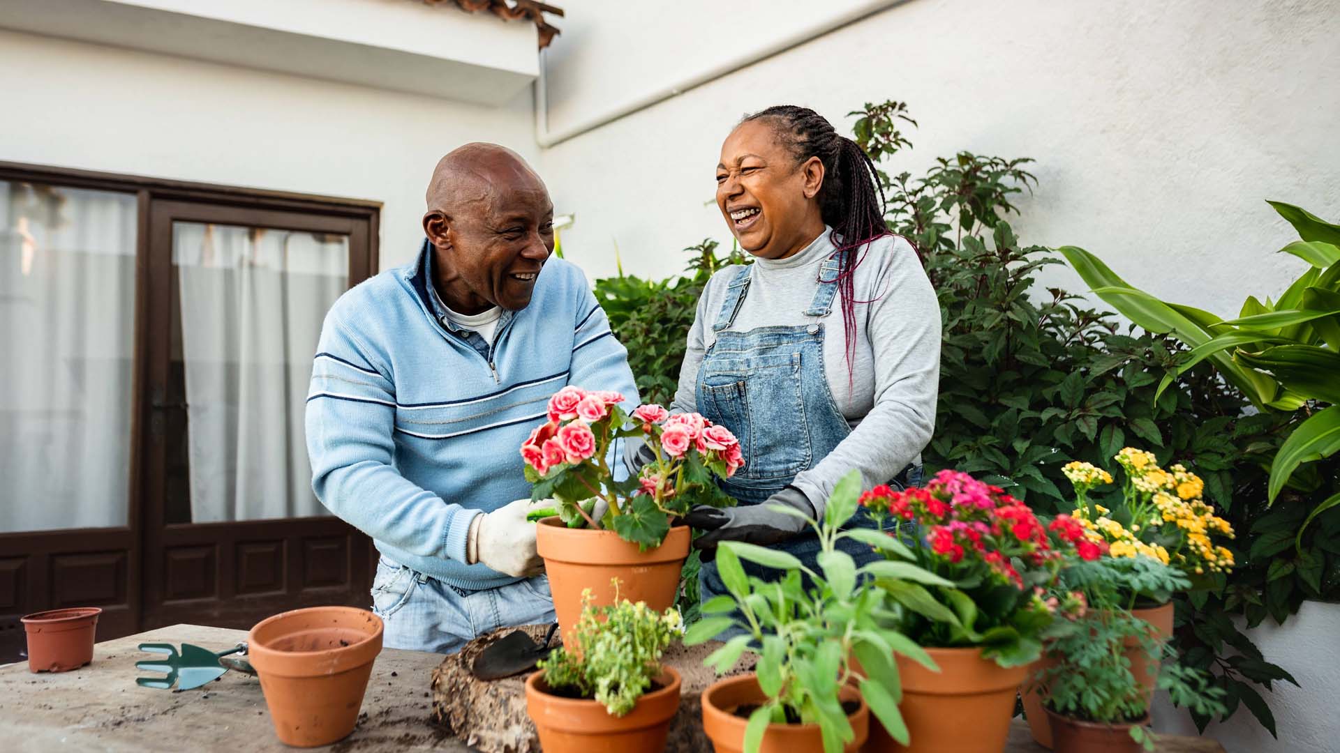 Two people gardening and smiling with pots of plants surrounding them. 