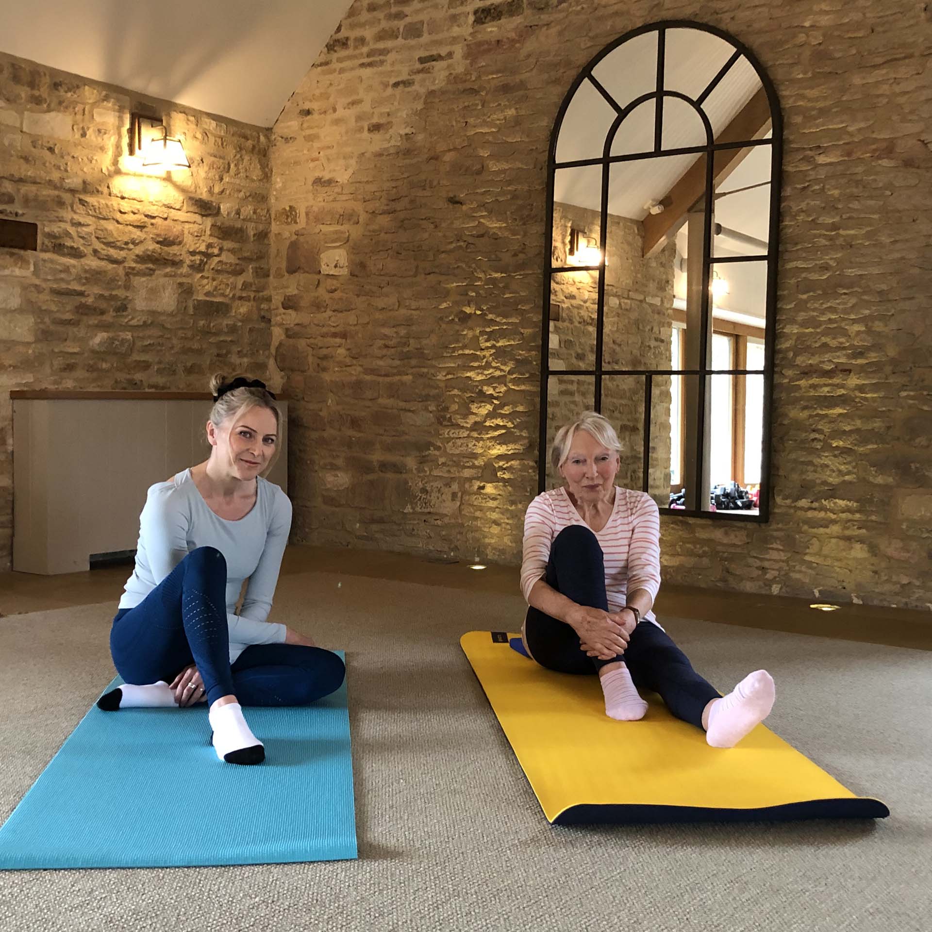 Two women sat on pilates mats in an exercise studio