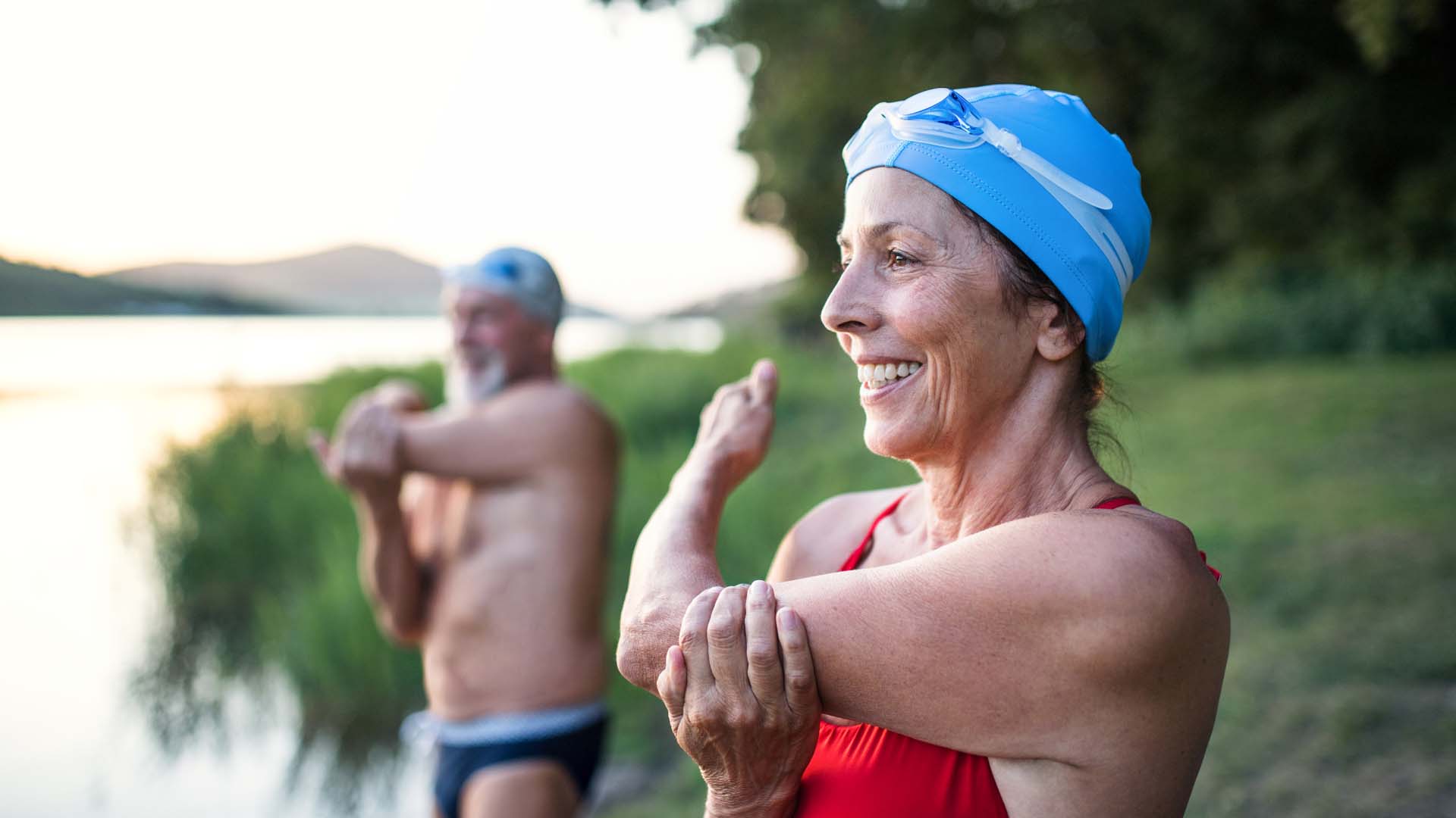 Male and female swimmers wearing caps and dressed for a swim, stand lakeside prior to their wild swim.