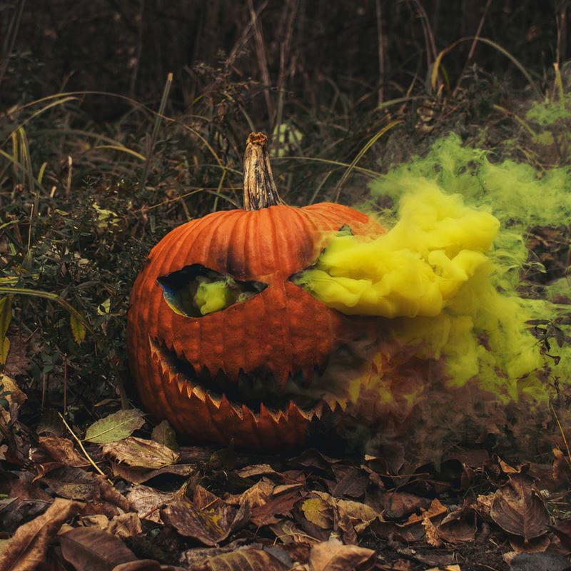 A carved pumpkin with yellow smoke pouring out