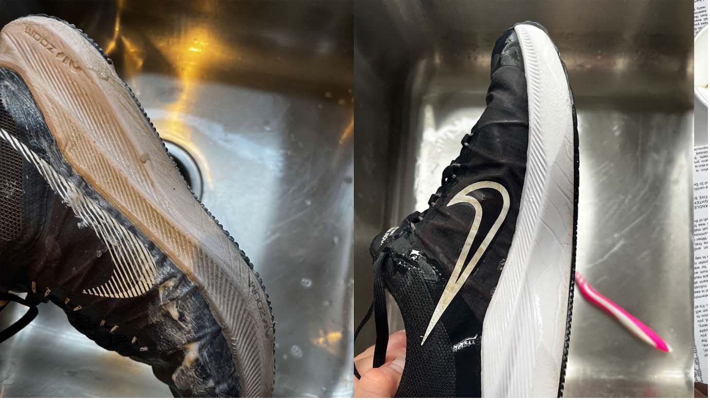 A black trainer with white sole being rinsed in a stainless steel sink