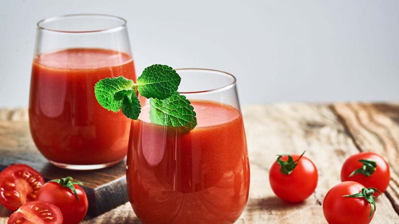 Two glasses of tomato juice surrounded by fresh tomatoes