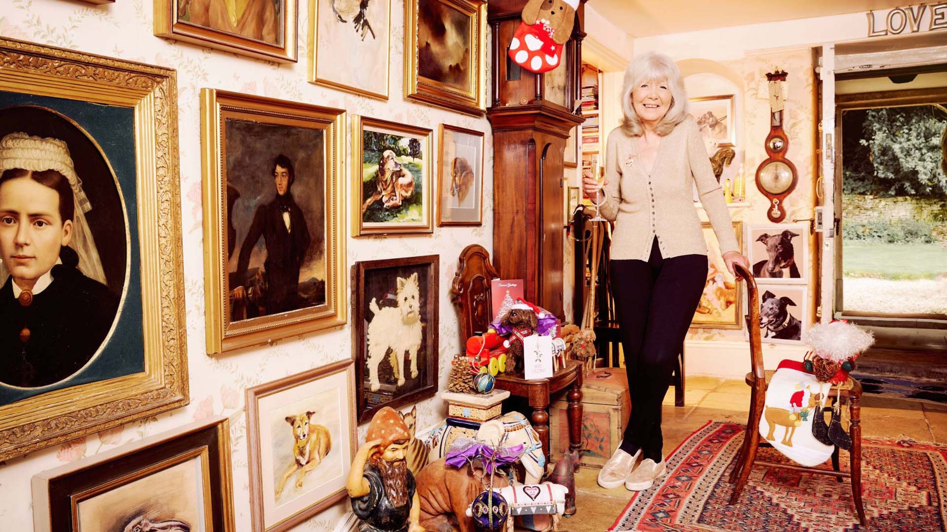 Jilly Cooper standing in her home with a glass of champagne
