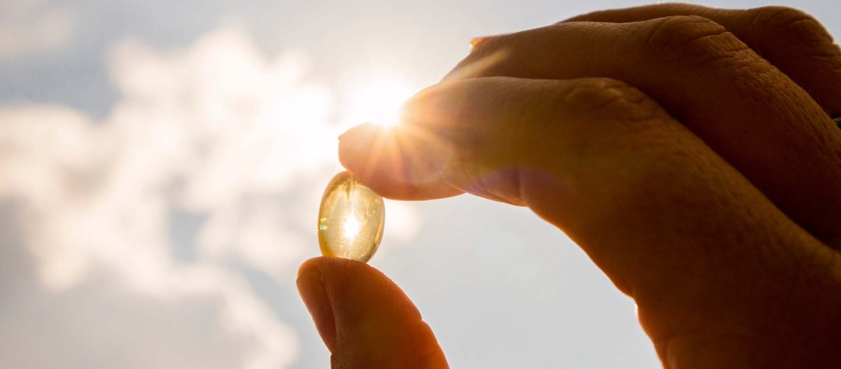 A Vitamin D capsule being held up to the sun between a man's finger and thumb