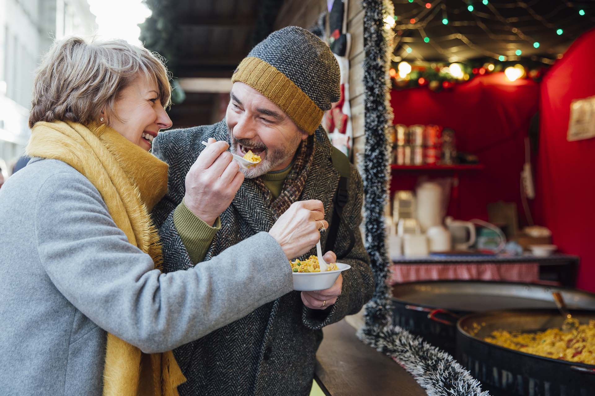 A man and a woman eating food at a street food stall in an open air market in winter