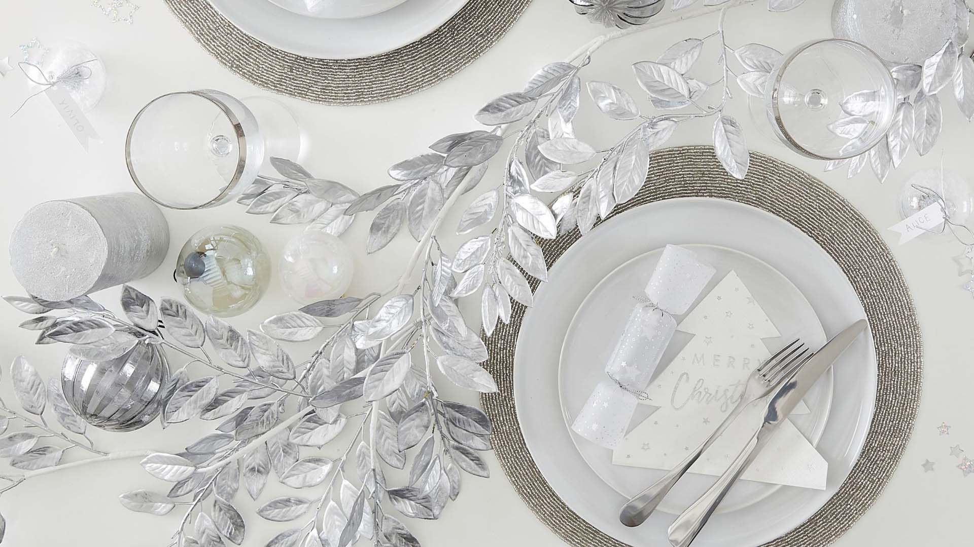 A festive table setting with silver accents including silver foliage, baubles and white Christmas crackers