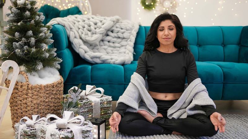 Woman sitting next to the Christmas tree doing yoga