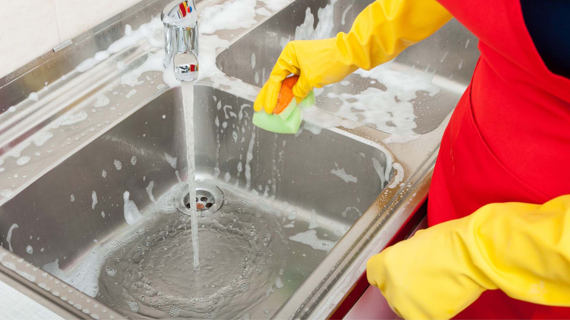 someone cleaning the kitchen sink with marigold gloves on