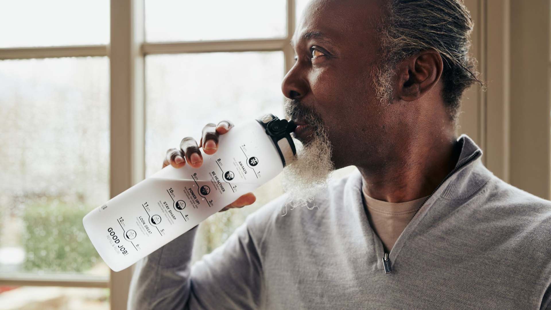 bearded man drinking from a water bottle by the window