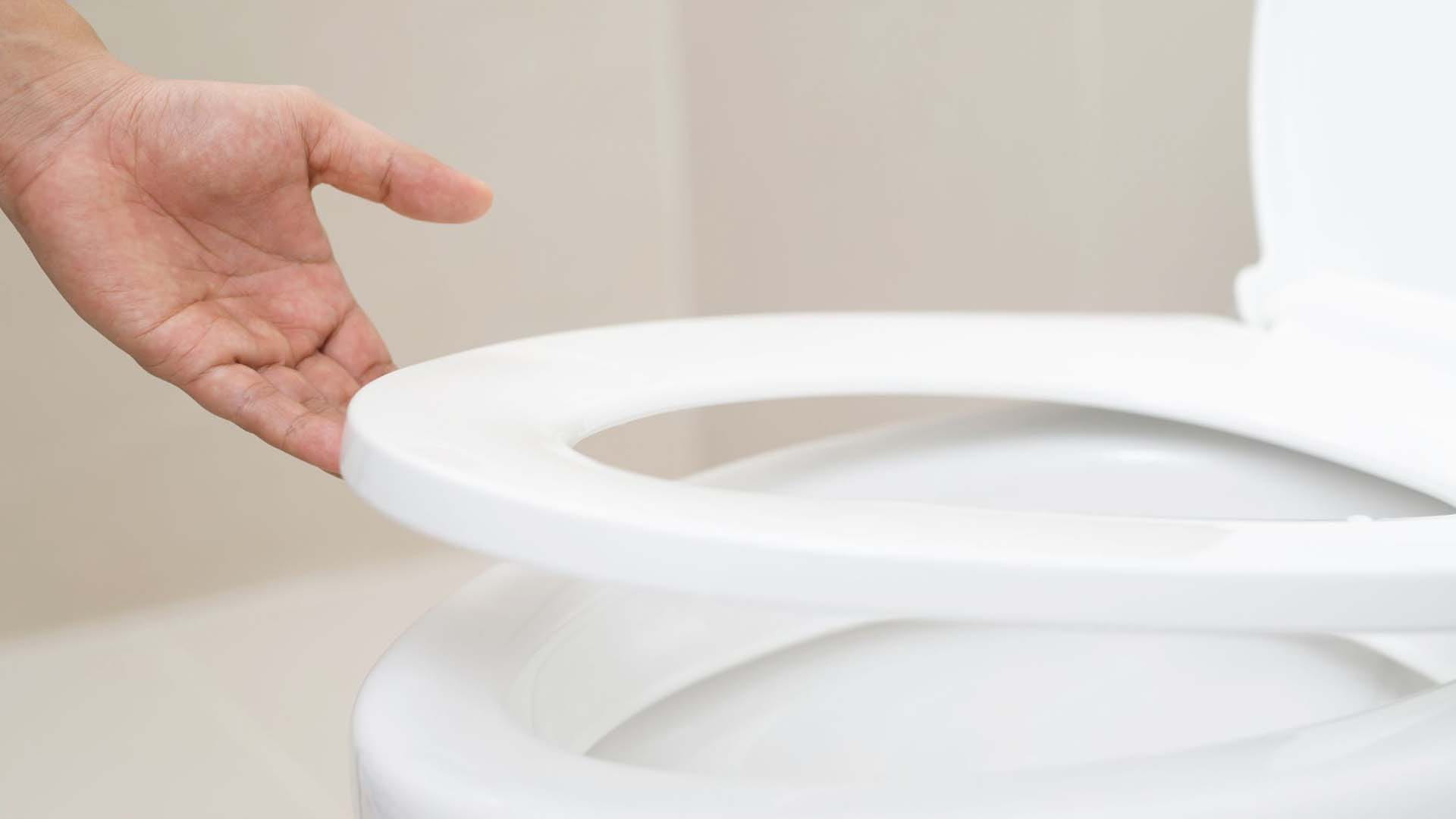 hand holding up a toilet seat slightly