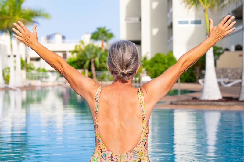 An older traveller celebrates holidaying solo at the pool