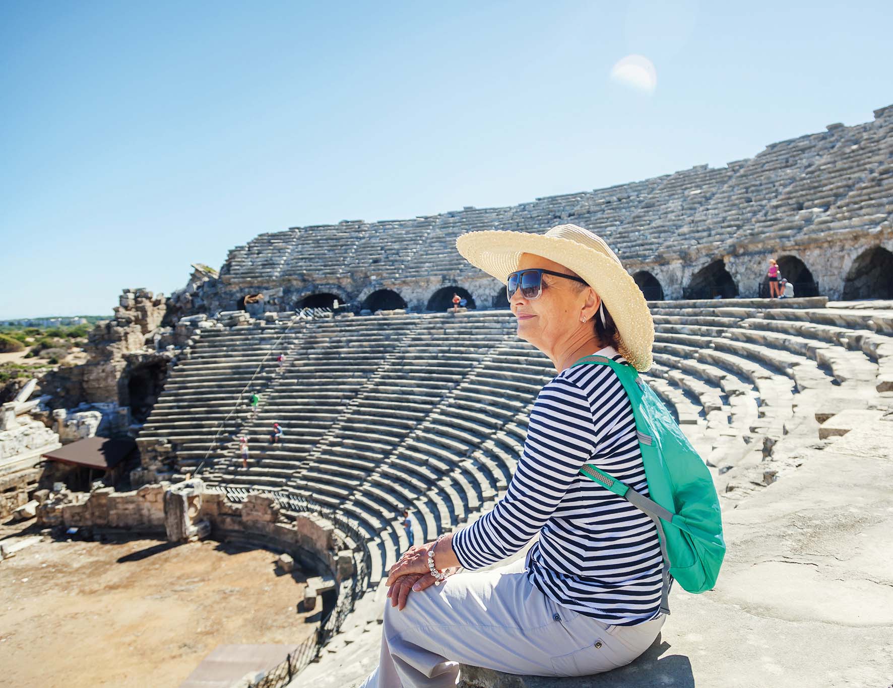 Mature beautiful woman traveler, sits on the steps of the amphitheater in admiring the view. Travel to Greece and Turkey, the monuments of ancient architecture, active seniors; Shutterstock ID 1018392475; purchase_order: HL0022871; job: SE Image collection download; client: Client STG; other: Holidays