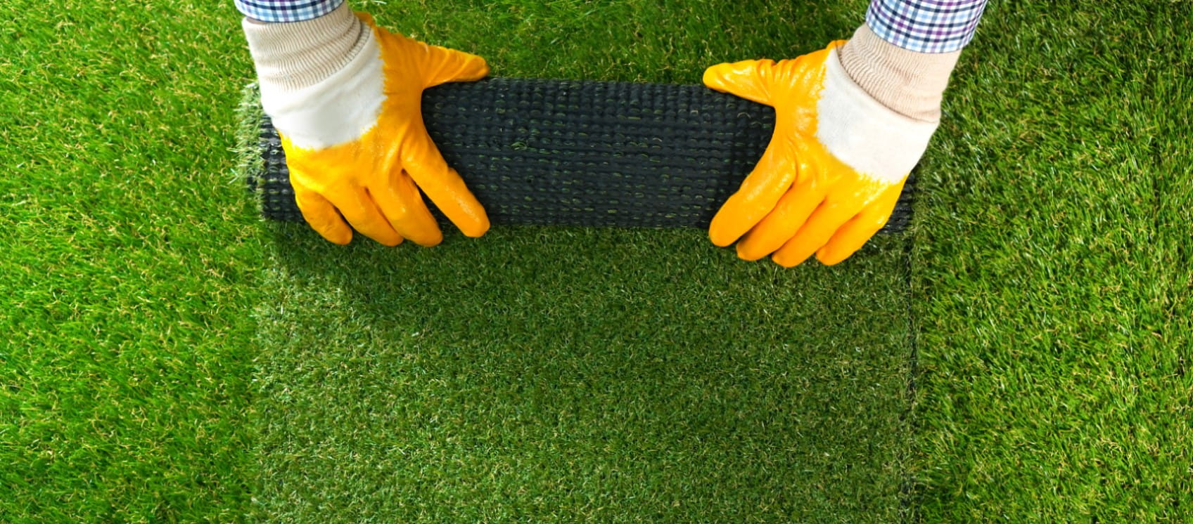 A man's hands hold a roll of artificial grass | Getty/Dmytro Varavin