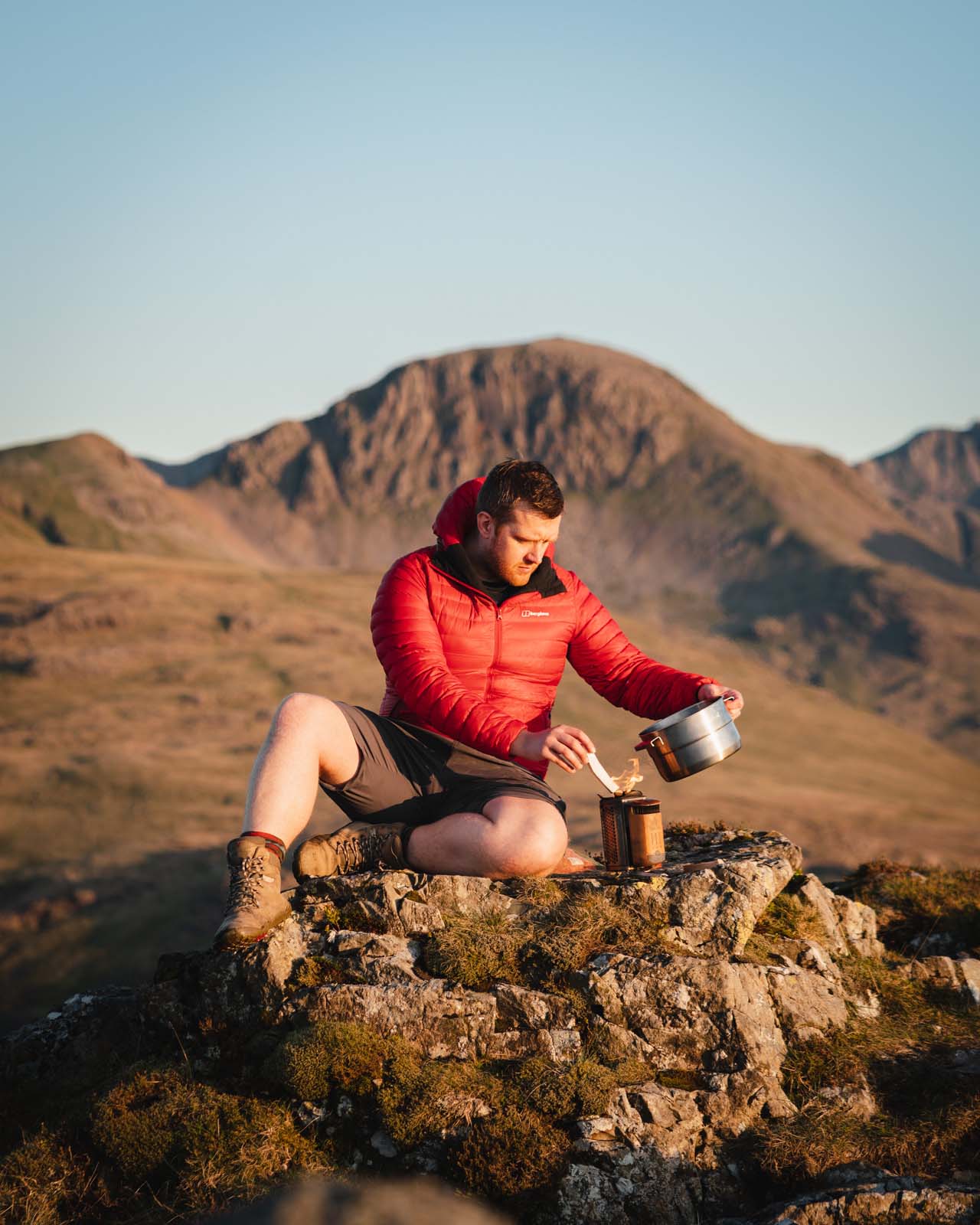 Harrison Ward, author of Cook Out, sitting on a rock in the hilly countryside eating from a flask