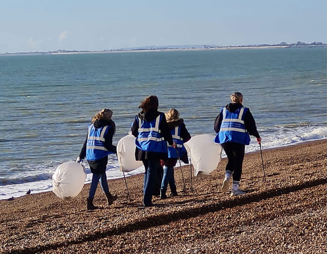 Group of four people walking along a beach with litter picking equipment