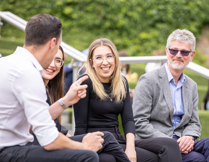 Four people sitting outside talking and smiling