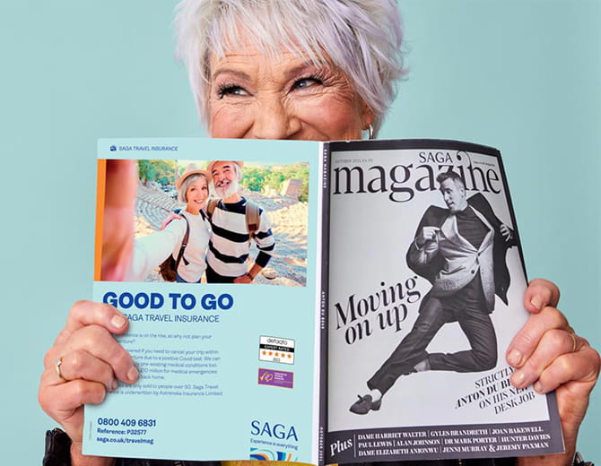 Person smiling holding an open issue of Saga Magazine