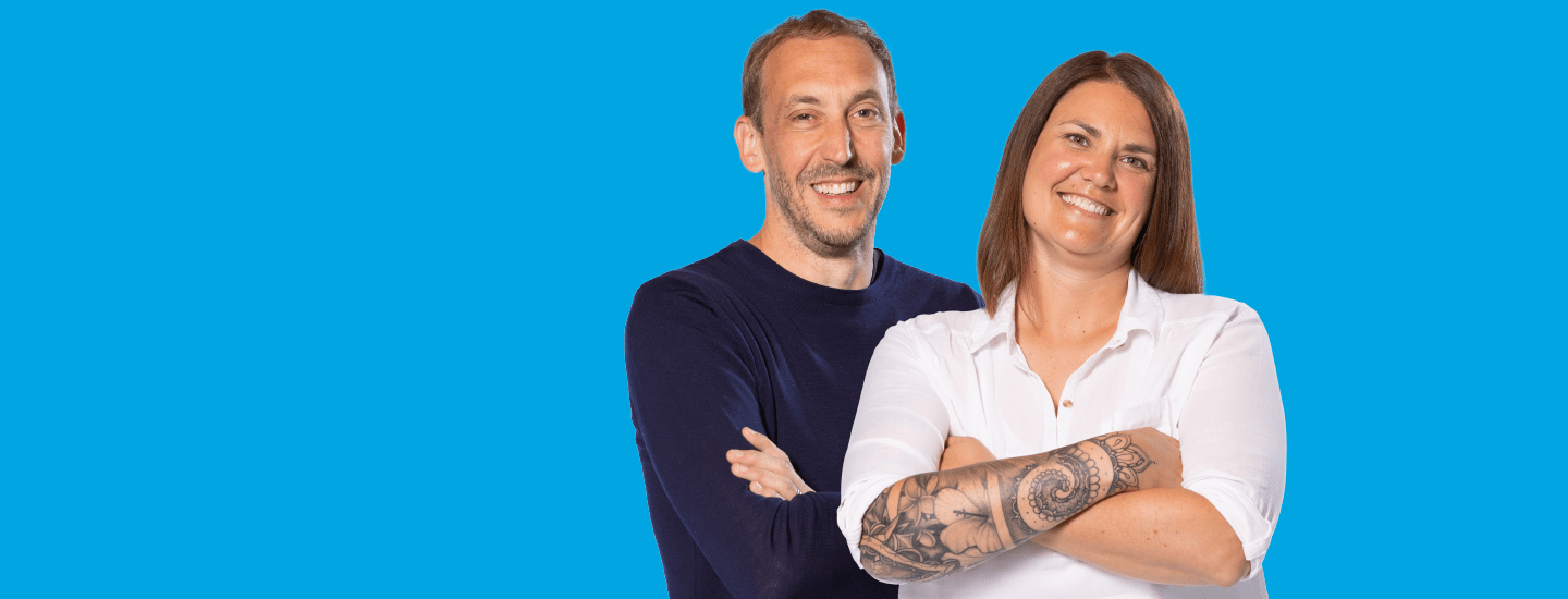 Two people standing back to back with folded arms and smiling on a blue background