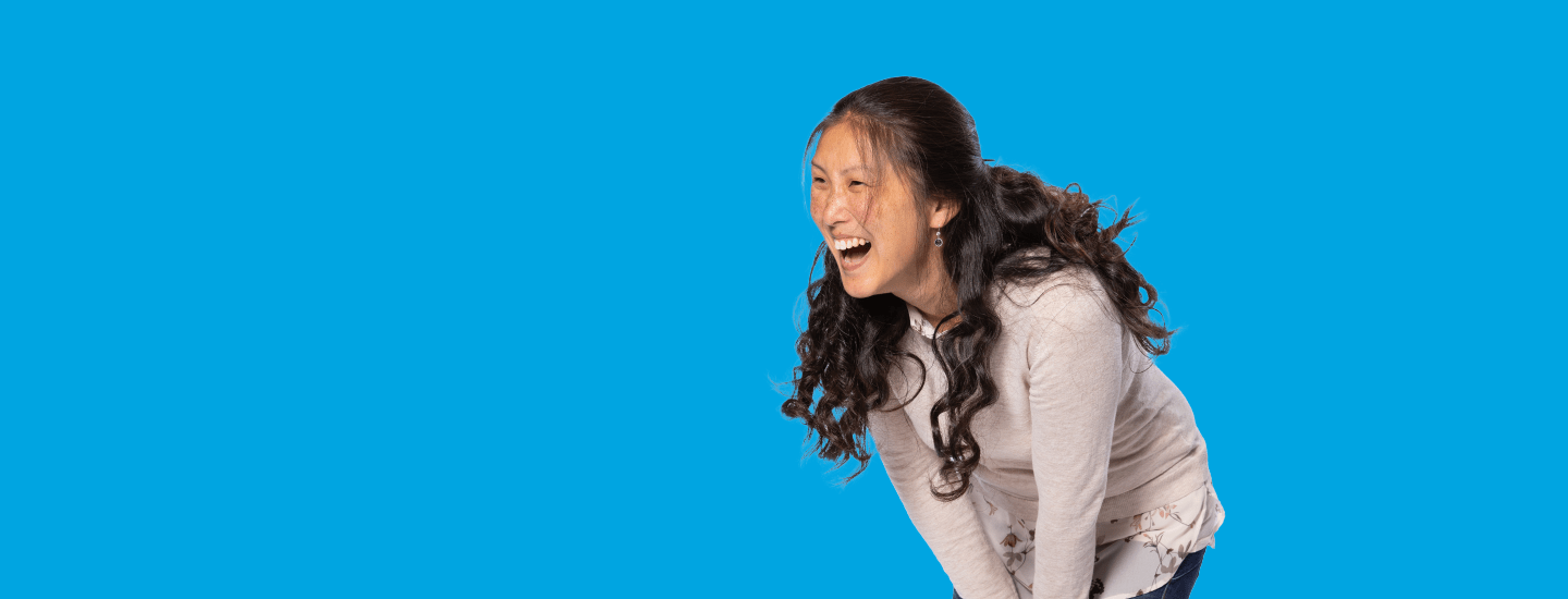 Person with long hair laughing against a blue background