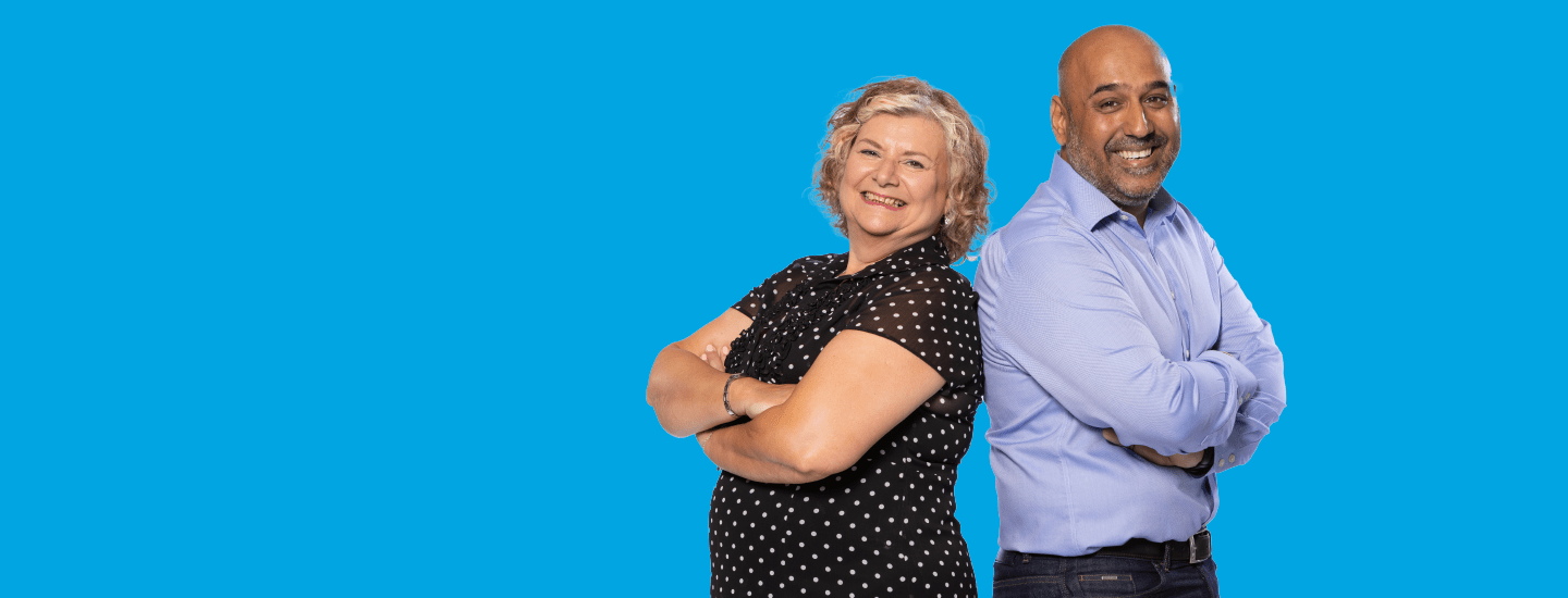 Two people standing back to back and smiling against a blue background