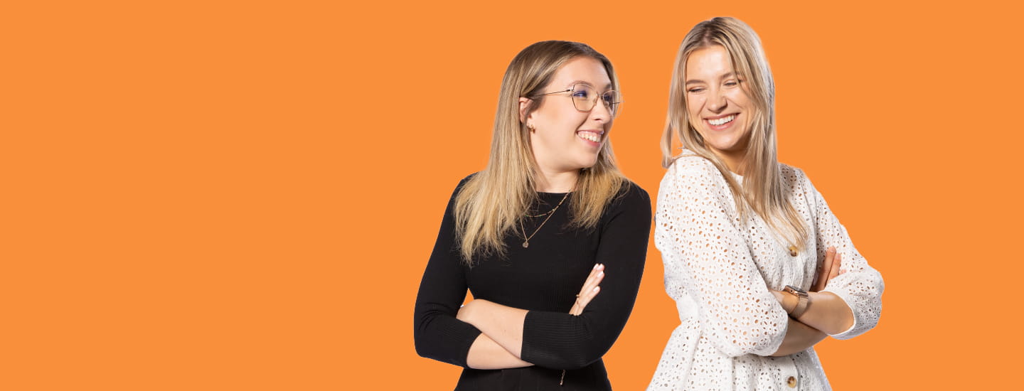 Two people standing back to back with their faces turned towards each other, smiling on an orange background