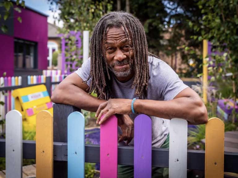 Man with crossed arms leaning on a colourful fence