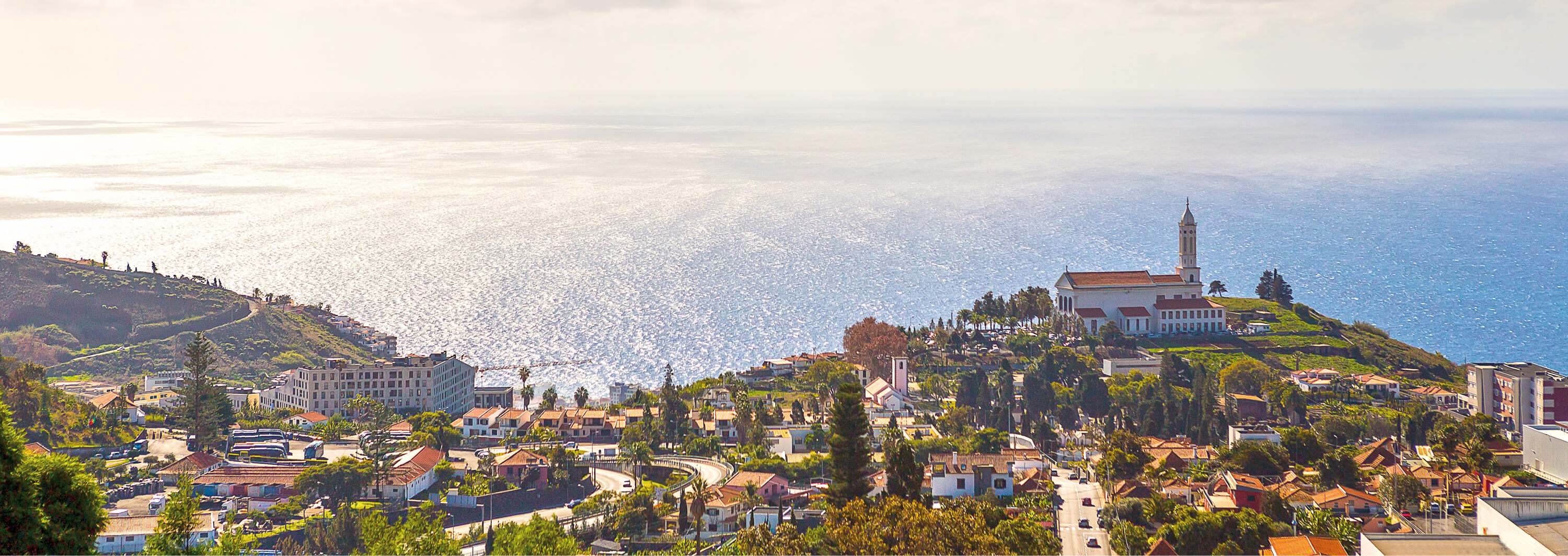 Coastal town overlooking the sea, with hillside homes and a hilltop church complex above the waterfront.