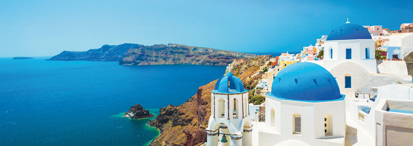 White buildings with blue domes overlooking the sea on a sunny Greek island.
