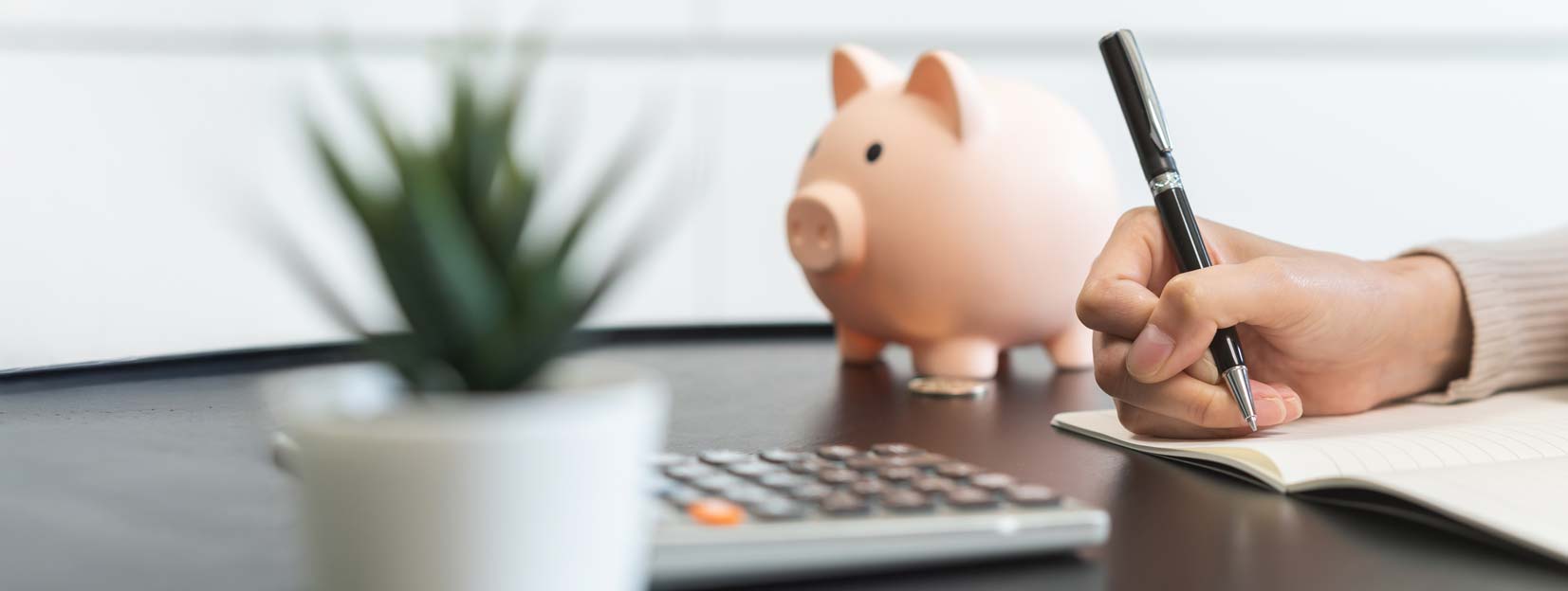 Hand writing in a notebook next to a calculator and a pink piggy bank, with a text box promoting budget insights from Saga Money.