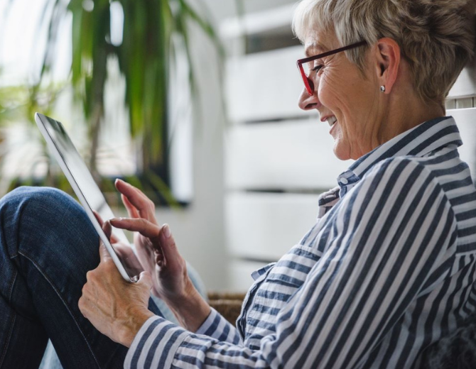 Older person wearing glasses and a navy and white striped shirt looking at a tablet