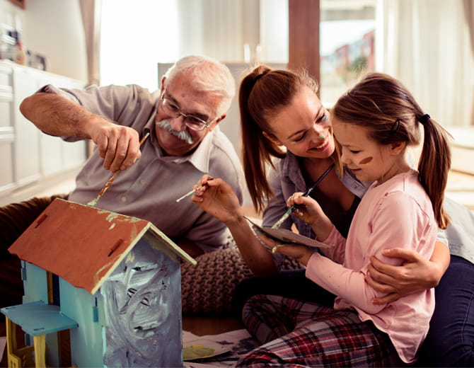 A grandparent with daughter and grandchild painting a small house