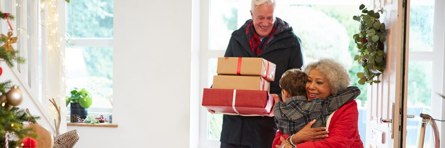 Grandparents arriving with presents at Christmas, hugging their grandchild
