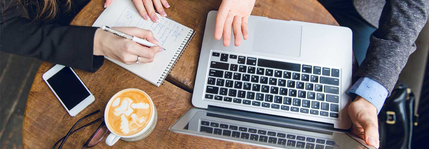 Aerial view of two people sitting a coffee table with a laptop and notepad