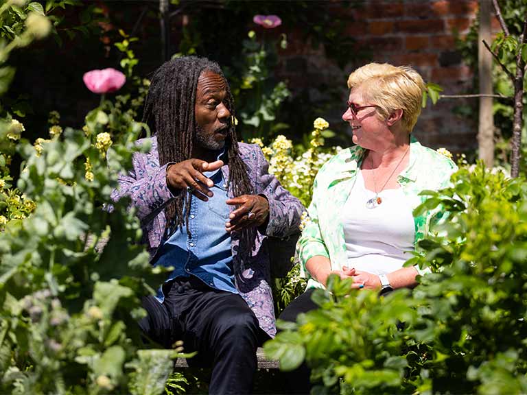 Danny Clarke and a lady in a garden sitting on a bench talking