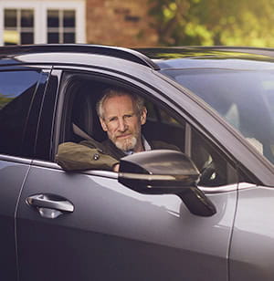 A mature man looking out of the driver side window of his car parked on his driveway