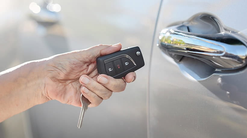 Close up of a woman's hand holding a car key next to the car door