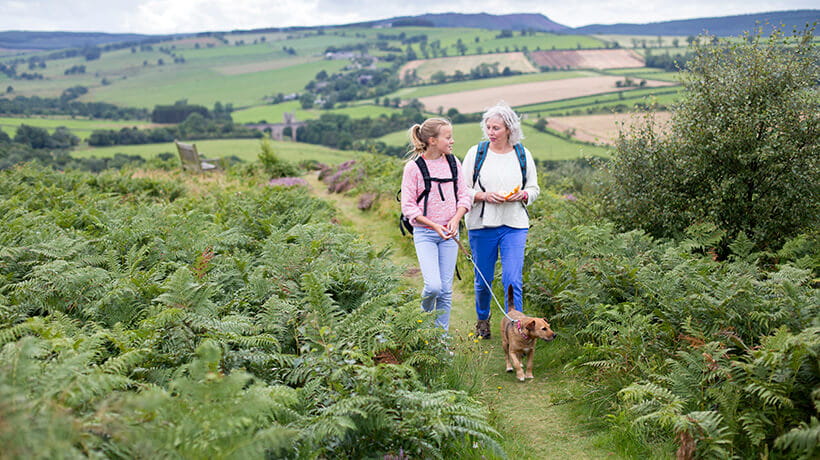 A woman walking her dog in the countryside with her granddaughter