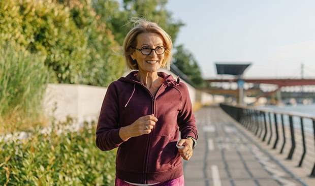 A mature woman running along a promenade on a sunny day.