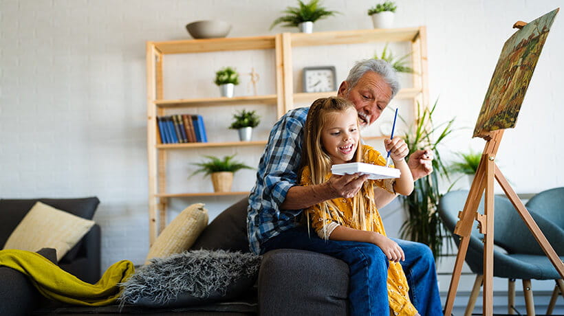 Senior man with child painting on canvas. Grandfather spending happy time with granddaughter