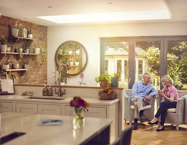 A mature couple discussing what they see on their phones while sat together in their modern kitchen