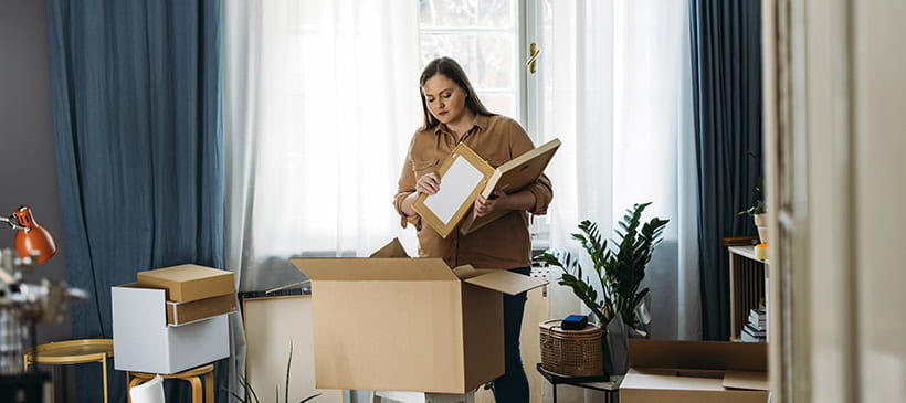 A young woman unpacks a box of personal belongings in a living room