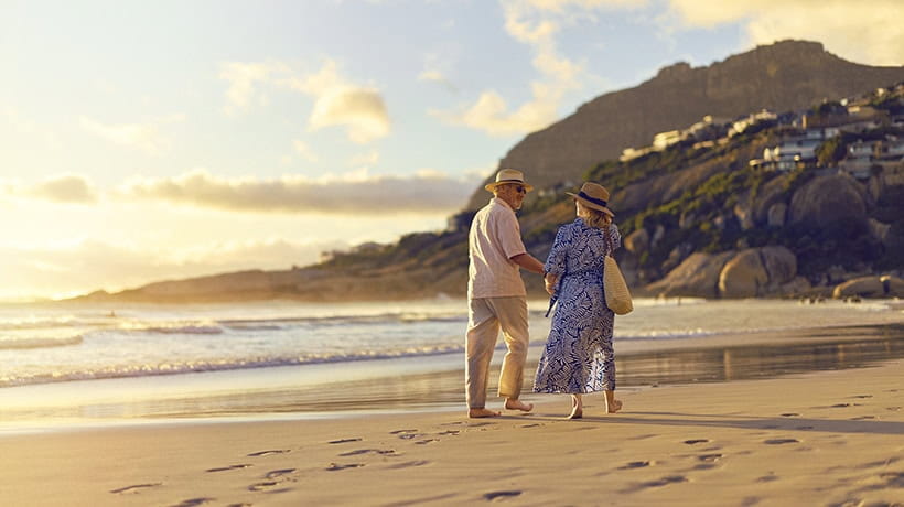 A mature couple walking along a sandy beach as the sun sets