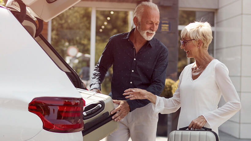 A mature couple packing luggage in their car at a hotel