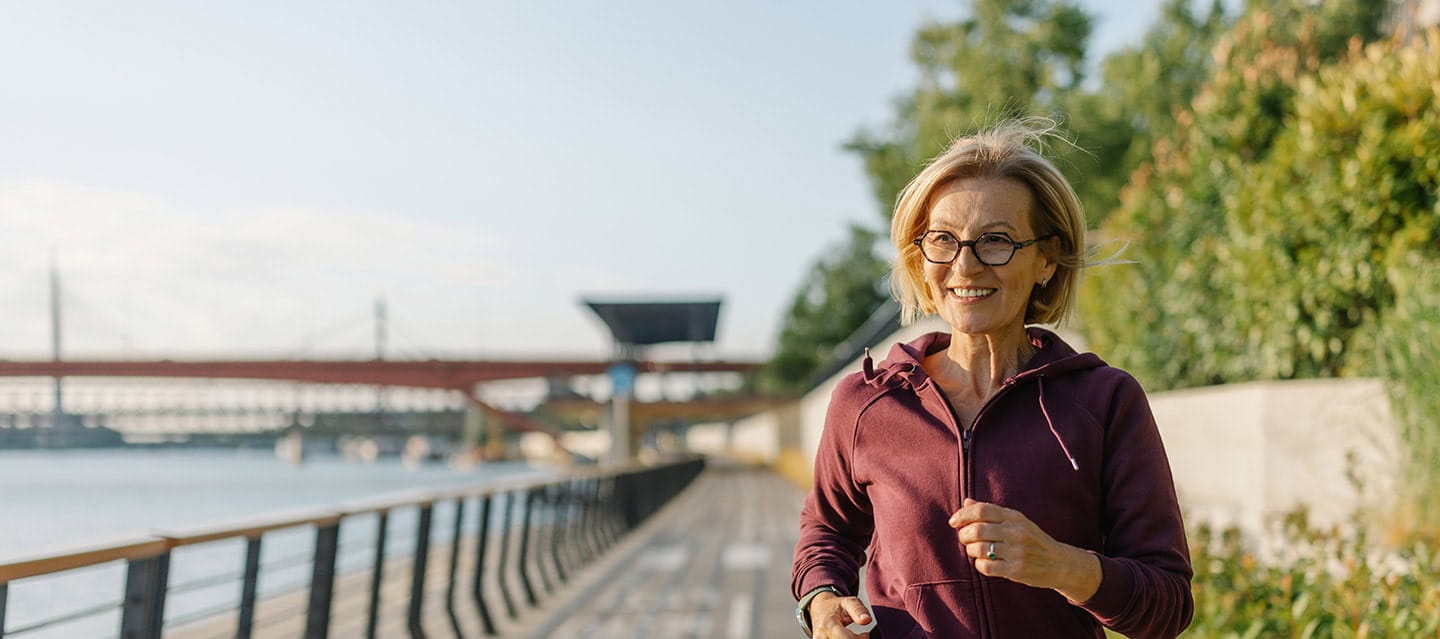 A mature woman running along a promenade on a sunny day.
