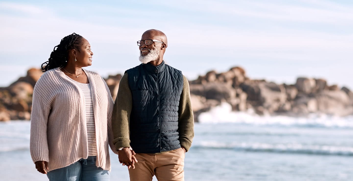 A mature couple walking along a beach holding hands on a chilly day.
