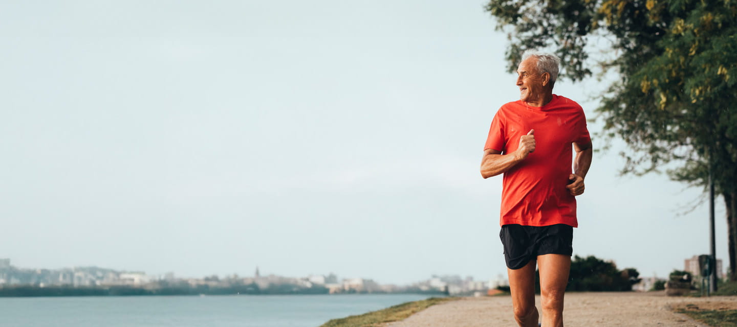A man in a red running top running on a footpath by a river